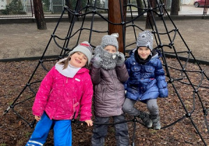 Trzy dziewczynki siedzą na pajęczynie do wspinania w ogrodzie przedszkolnym